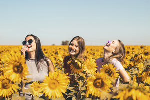 Best friends wear Nözscreen laughing in sunflower field. Reef safe dermatologist recommended zinc oxide SPF sunscreen for face